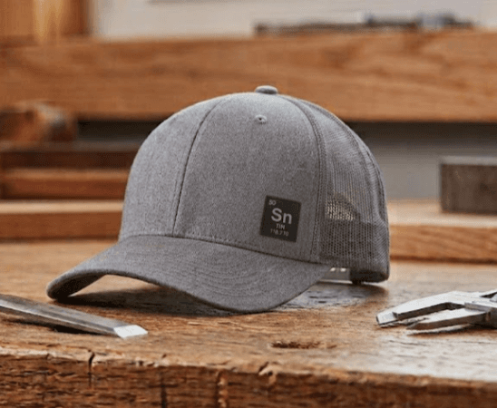 Front product photo of the Anodize Sn cap, a gray six-panel mid-profile Richardson 112 trucker with a visible 1 inch by 1 inch Sn tile on the front lower-right panel